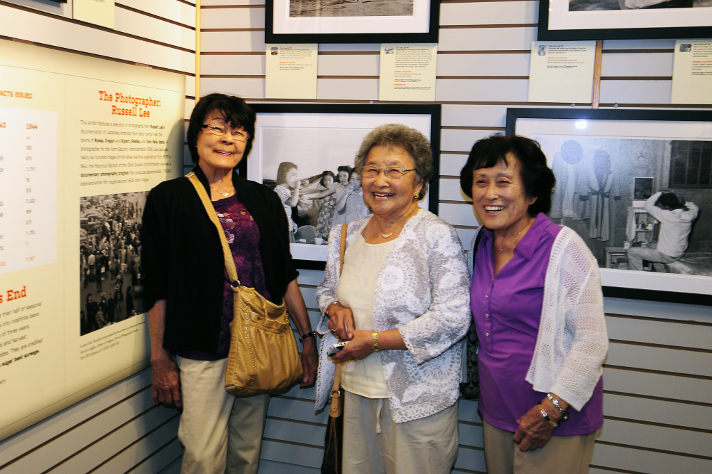 Anne Enoki, Rose Sorensen, and Kay Yamaguchi stand in front of the image Russell Lee took of them at the Nyssa camp in 1942. Photo courtesy of David Nishitani.